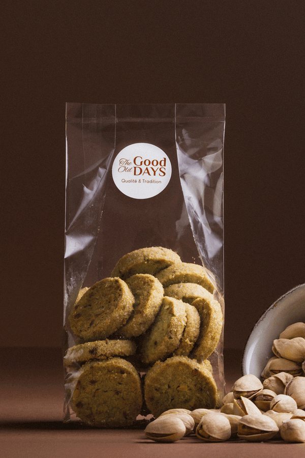 Sablé pistache The Good Old Days dans son emballage, posé avec des pistaches entières sur fond brun.
