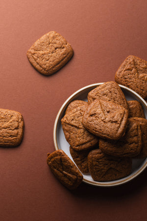 Spéculoos présentés dans une assiette sur fond brun, biscuits empilés