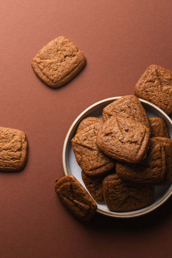 Spéculoos présentés dans une assiette sur fond brun, biscuits empilés